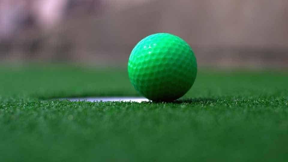 A green golf ball rests on green astroturf