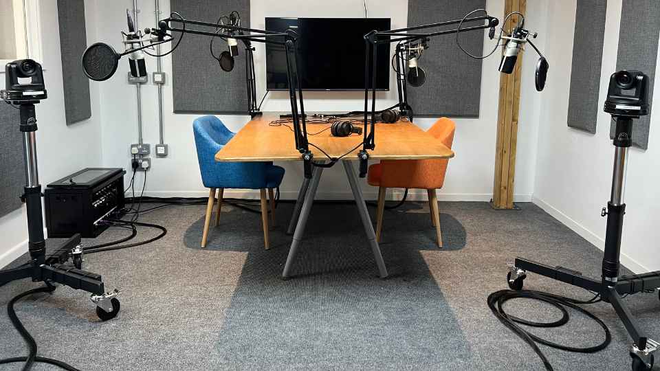 Picture of a podcast studio with two microphones and two chairs, with a screen behind the table