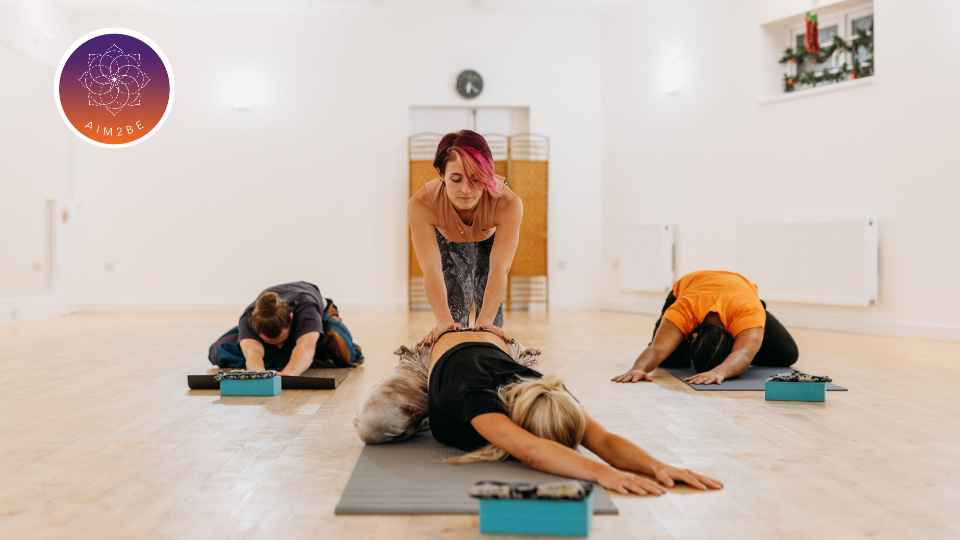 Group of people doing yoga with the instructor helping an individual.