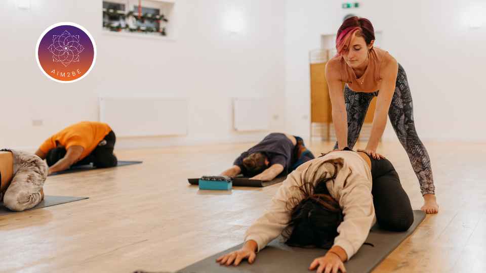 A group of people in a yoga class with the instructor helping an individual.