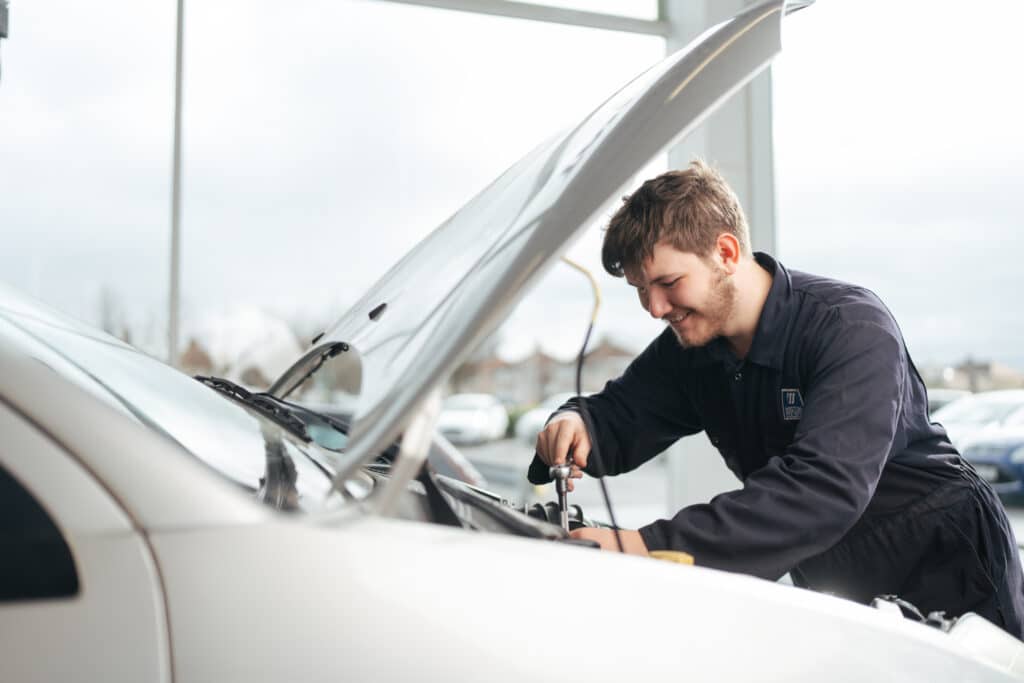 Apprentice mechanic working on a white care that has an open bonnet