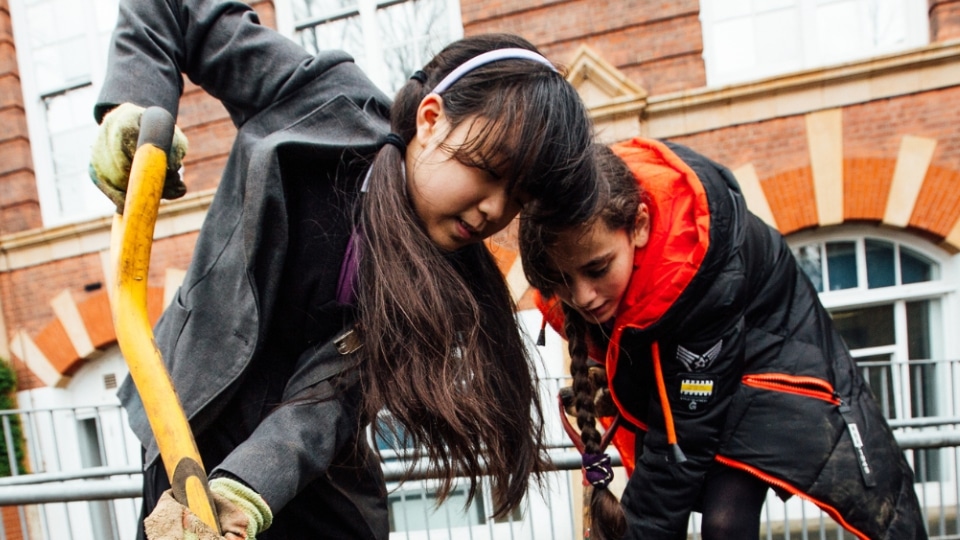 Two children digging outside a school building.