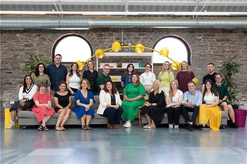 Group of people in business casual clothing sit on a sofa in a studio, the Ambitious PR team
